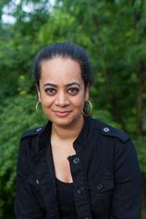 An image of the author, Priyanka Champaneri, wearing a black jacket with a high collar and large gold hoop earrings